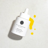 White skincare serum bottle with yellow droplets on a light gray background