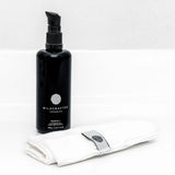 Black bottle labeled 'Wildcrafted Organics' with a white cloth and silver tool on a white background