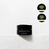 Black jar labeled 'Wildcrafted' on a white background with two awards above it.