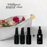 Set of black bottles withWildcrafted Organics branding, a white dish with flowers, and 'Wildflower travel ritual' text on a light gray background.