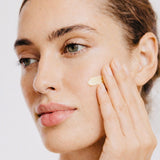 Woman applying cream to her face with a neutral background