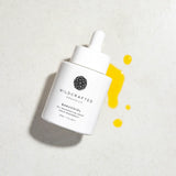 White skincare serum bottle with yellow droplets on a light gray background