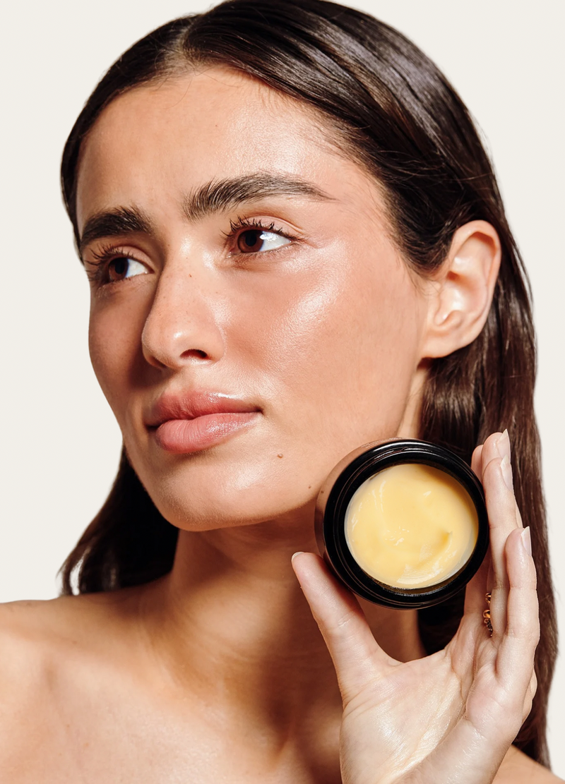 Woman holding a jar of skincare product against a neutral background