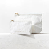 Two white pouches with gold zippers on a light gray background