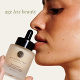 Wildcrafted Organics Wild Pansy serum bottle held close to a person's face with 'age less beauty' text.