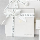 Gift box with a white ribbon featuring 'Wildcraft Organics' branding on a light gray background.