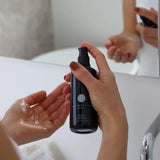 Person holding a black bottle labeled 'D'crafted' over another person's hand with soap on a white surface.