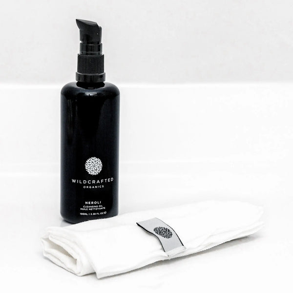 Black bottle labeled 'Wildcrafted Organics' with a white cloth and silver tool on a white background
