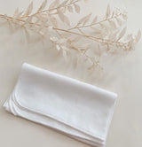 Folded white fabric on a light beige surface with a branch of leaves.